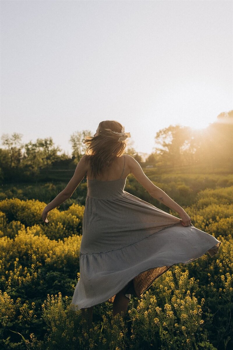 Cinematic wedding photographer twirls in field of gold flowers at sunset.