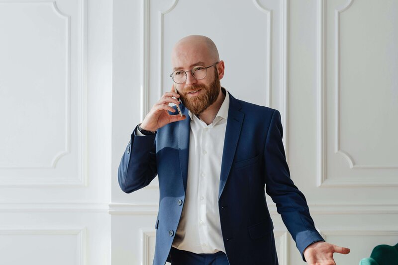 A businessman with a beard dressed in a blue suit, talking on his cell phone,  exuding a poised and confident demeanor.