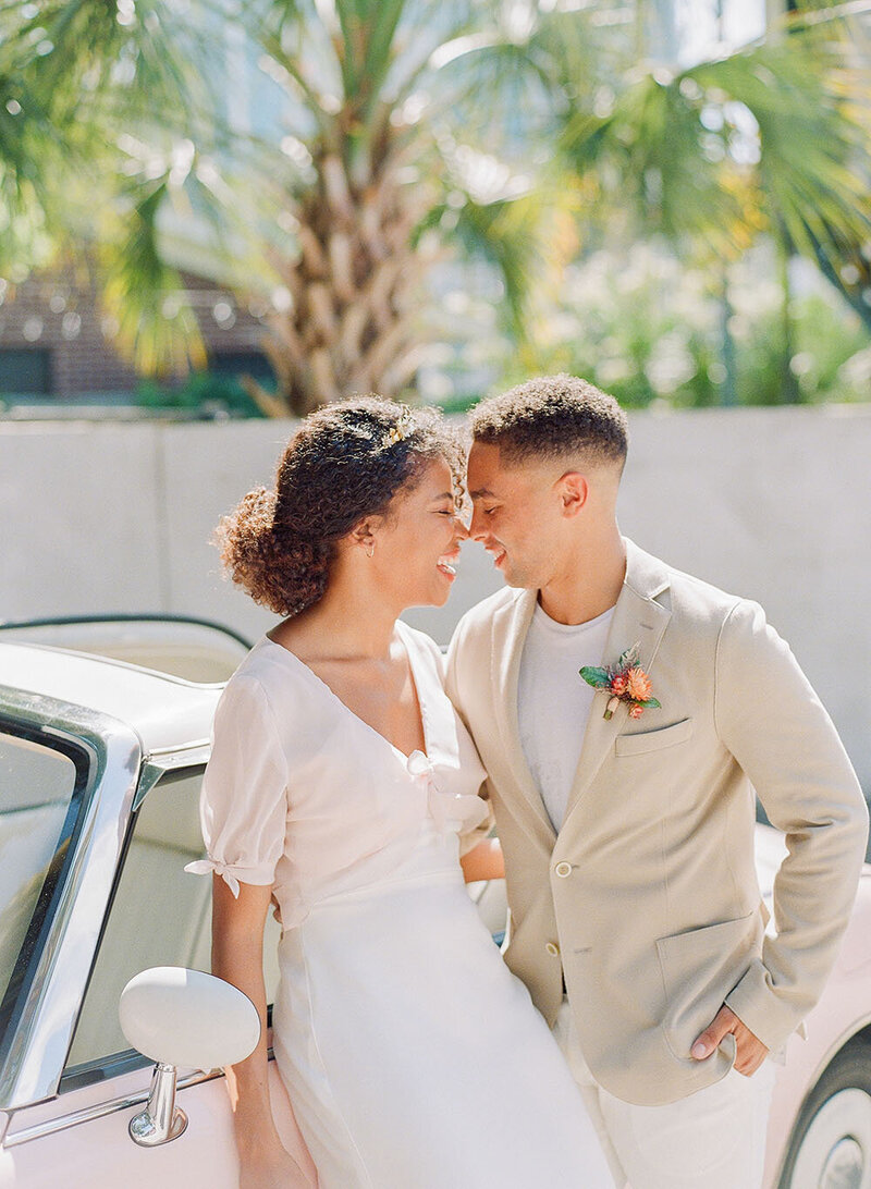 Playful eskimo kiss during newlywed portraits with a vintage pink fiat