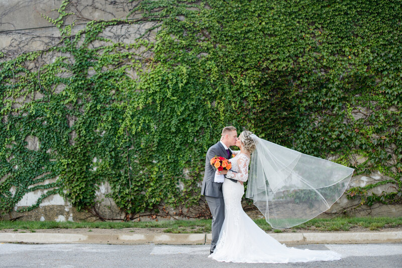 Bride and Groom kissing in front of gorgeous large wall full of greenery