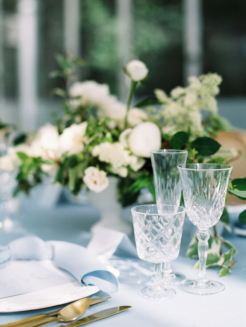 table with crystal glasses with white flowers and gold silverware