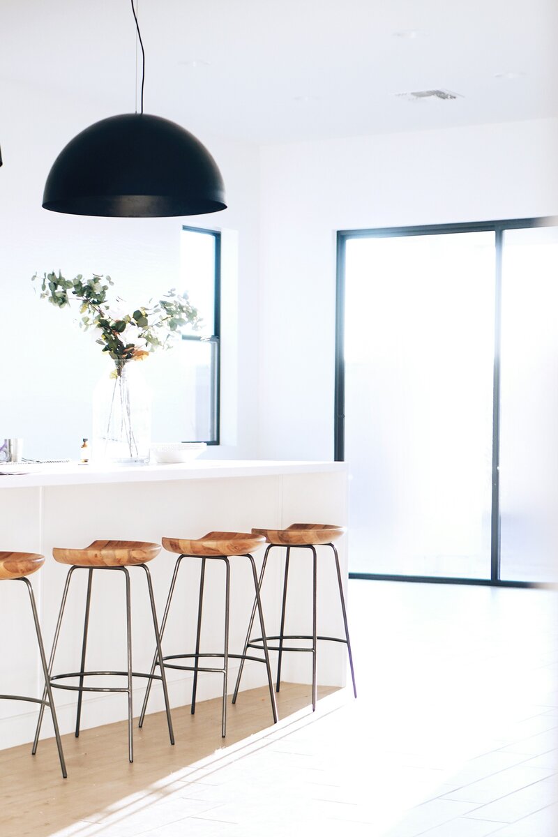 A modern kitchen with a sleek white counter top and stylish black pendant lights hanging above.