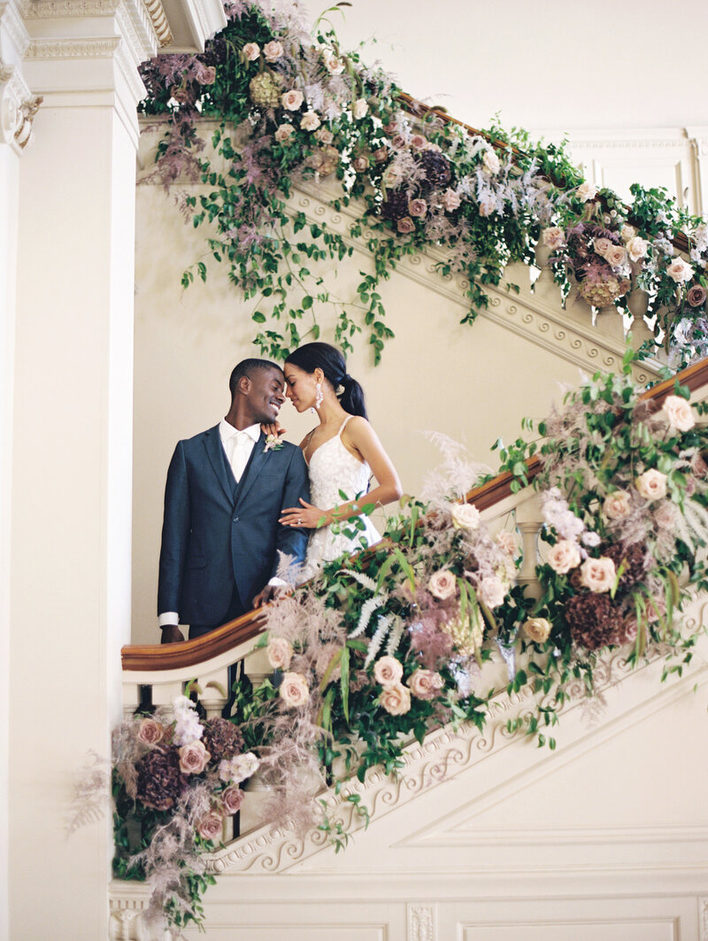 A wedding portrait of a couple going down the steps surrounded by flowers.