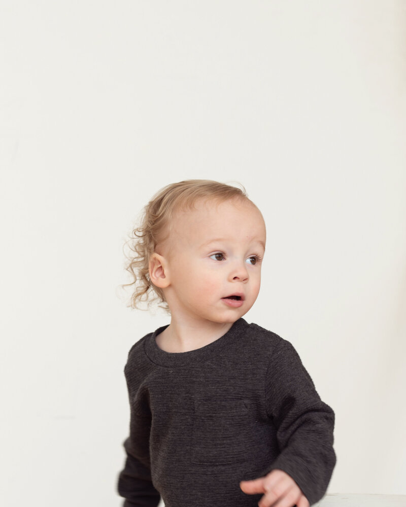 two year old in black shirt and jeans on white wall