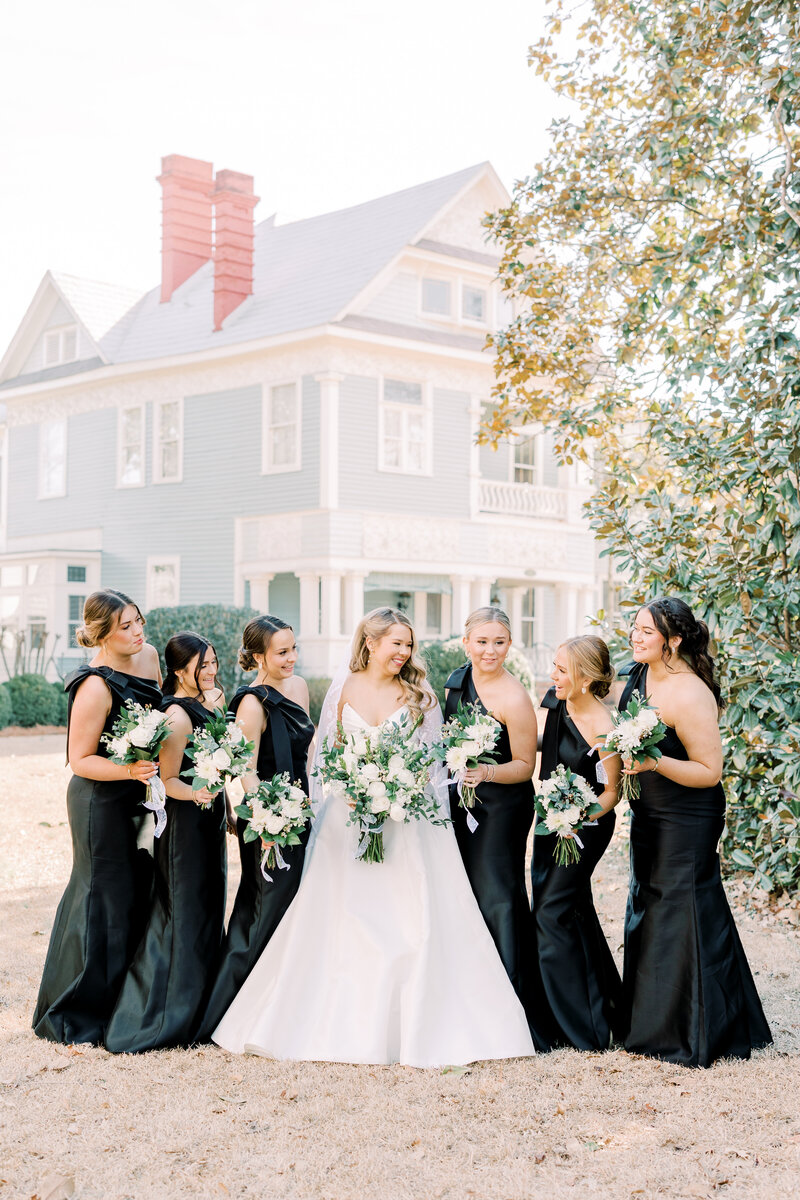 Bride standing outside with bridesmaids in black dresses holding white bouquets