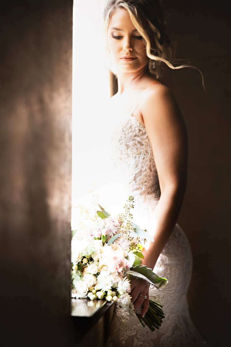 a bride standing in front of a window in her dress as an example of the importance of answering how to pick a wedding photographer
