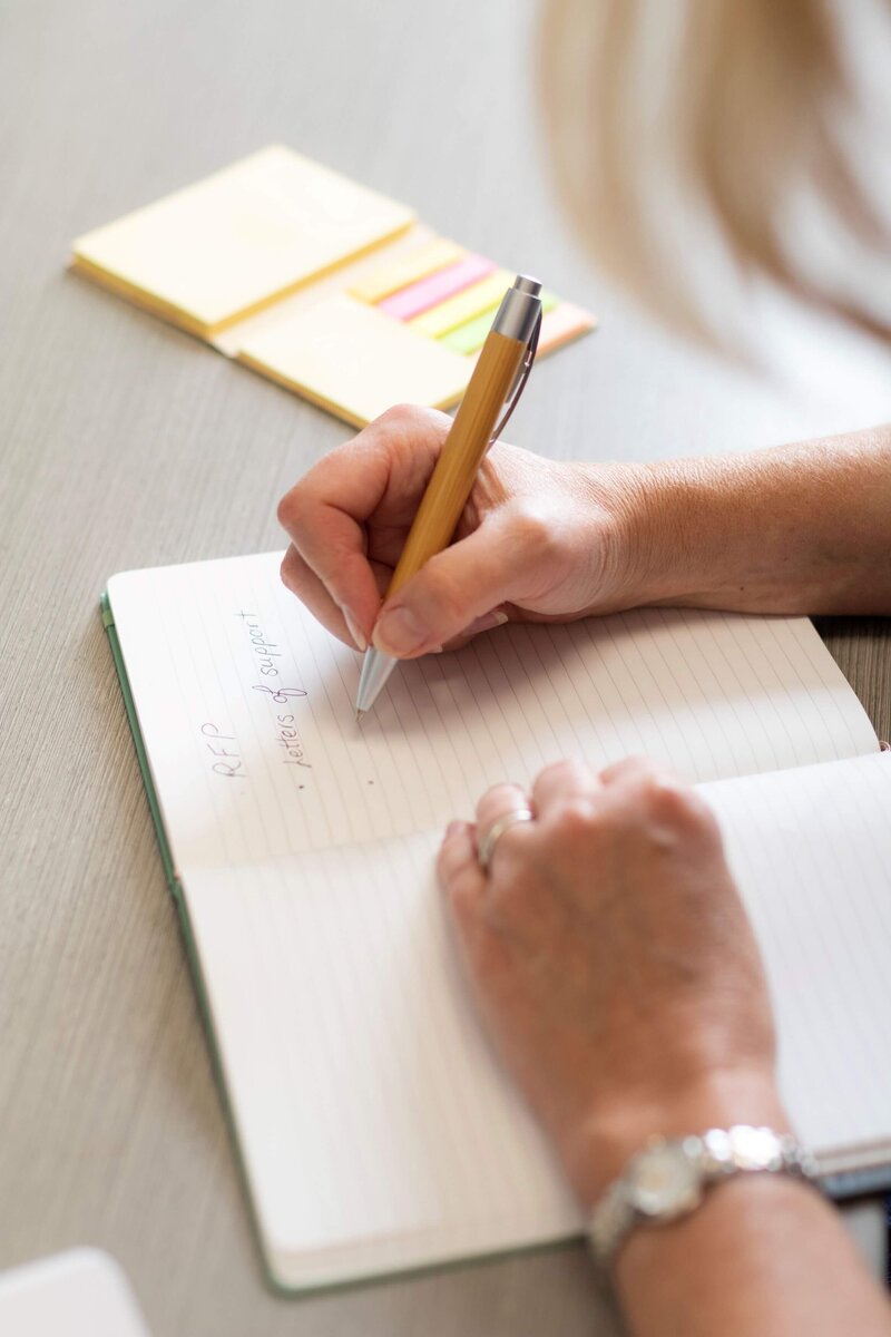 Hands writing grant writing plan in notebook
