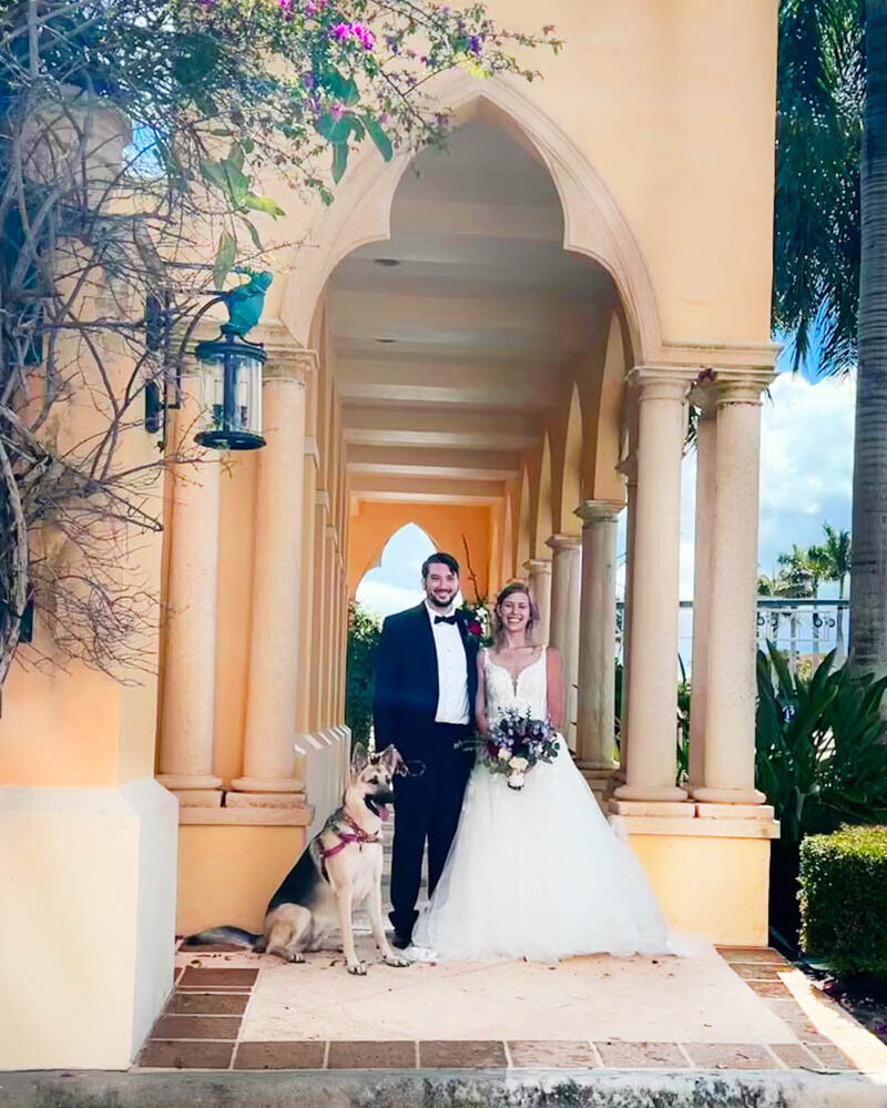 bride and groom standing in front of yellow arches with their german shepherd who is a dog of honor.