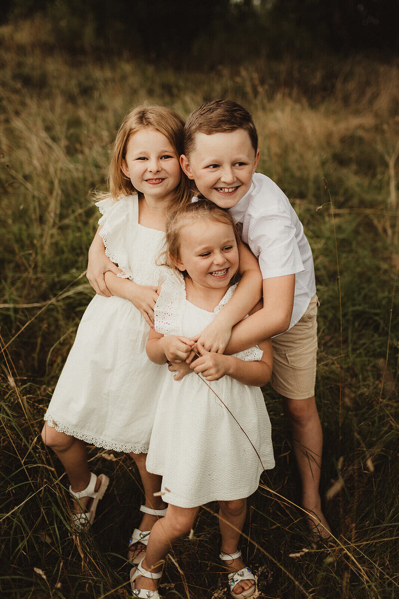 Siblings standing in long grass smiling during Hereford family photoshoot