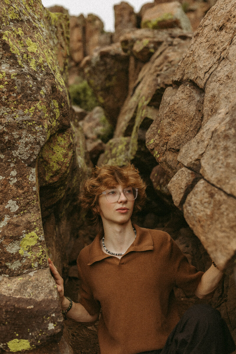 Senior boy with fluffy hair and a retro orange shirt in a cave.