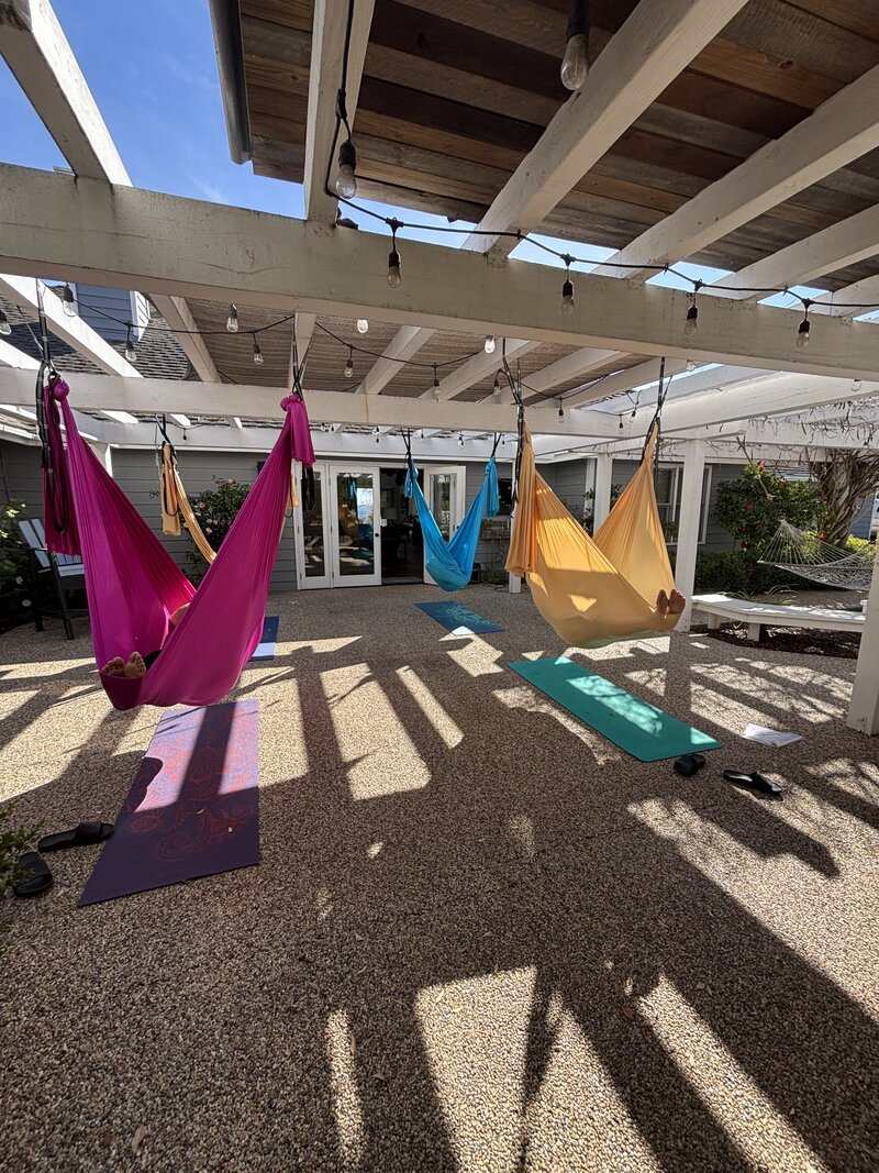 Bright colored somatic swings with people in them hanging from a pergola. 
