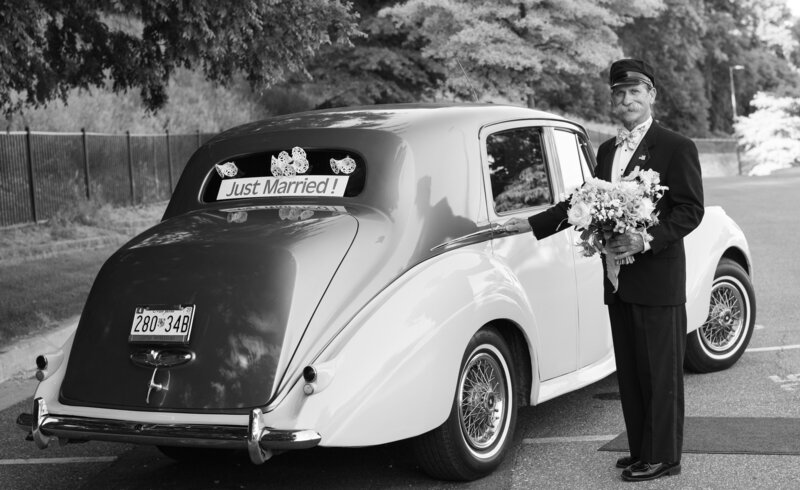 black and white photo of valet waiting for bride and groom at car