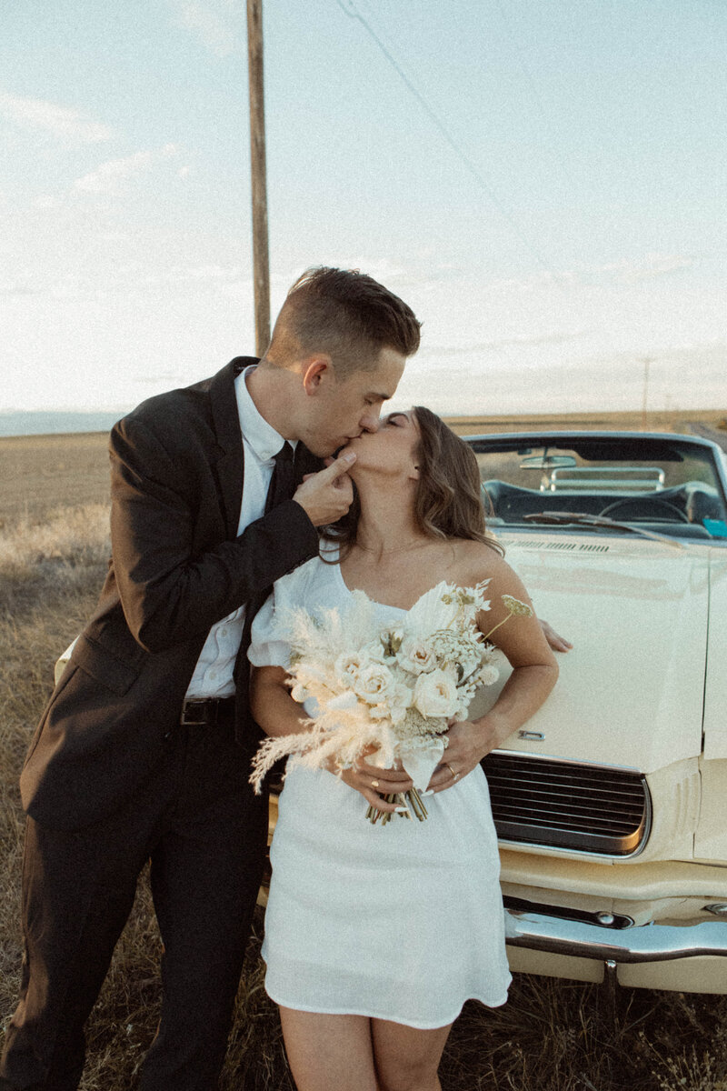 bride and groom kissing in front of a car