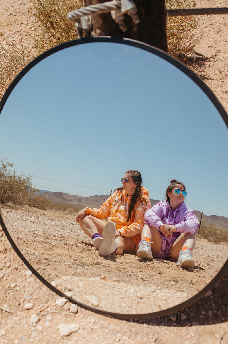 Two girls sitting on the ground reflected in a mirror.