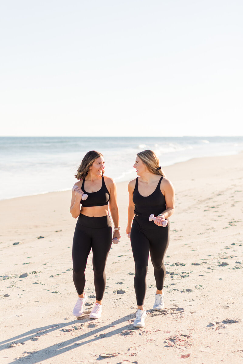 Two women walking on a beach holding weights