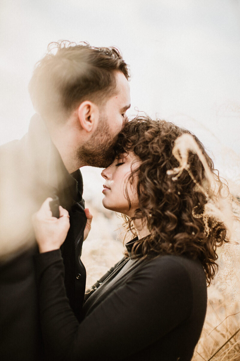 Man kissing a womans forehead as she pulls him closer in a field