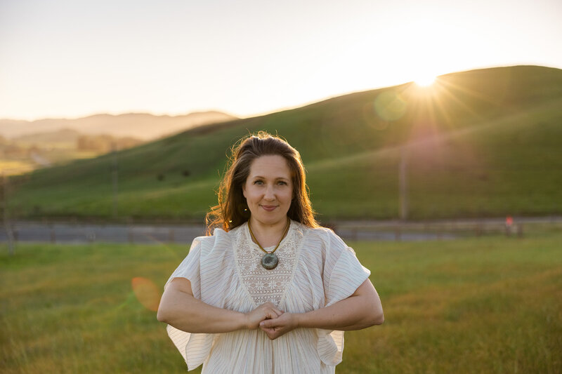Spiritual healer holding her hands together looking at the camera in the golden hills of California during golden hour