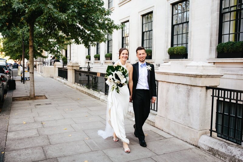 Romantic stroll: Couple walking through East London, bride with flowers.