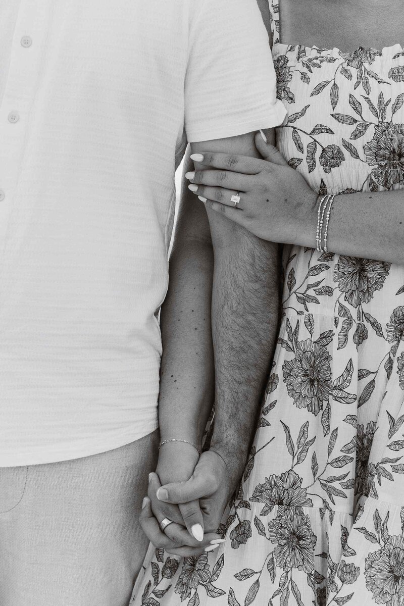 Greyscale close up of couple holding hands and woman's engagement ring