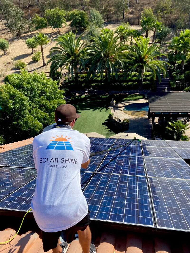 A skilled technician from Solar Shine SD cleaning solar panels on a residential roof, improving energy production with safe and effective cleaning techniques.