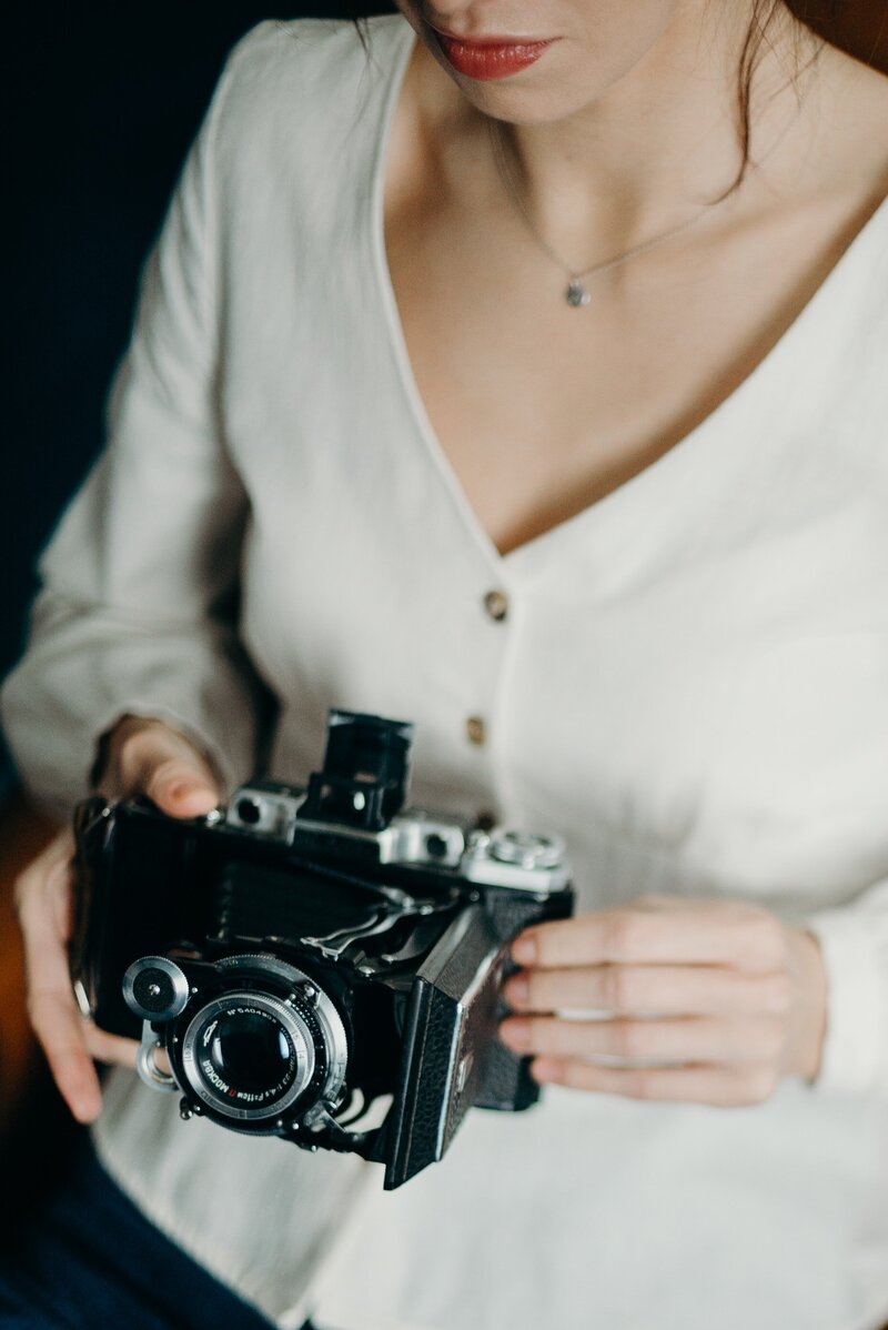 Lifestyle photography woman holding camera in white shirt with black background  in Tampa Bay, Florida Nadine B Photography