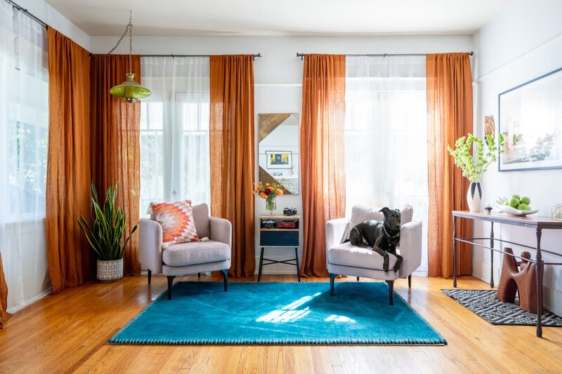 modern styled apartment with orange curtains, a blue rug, and two white chairs