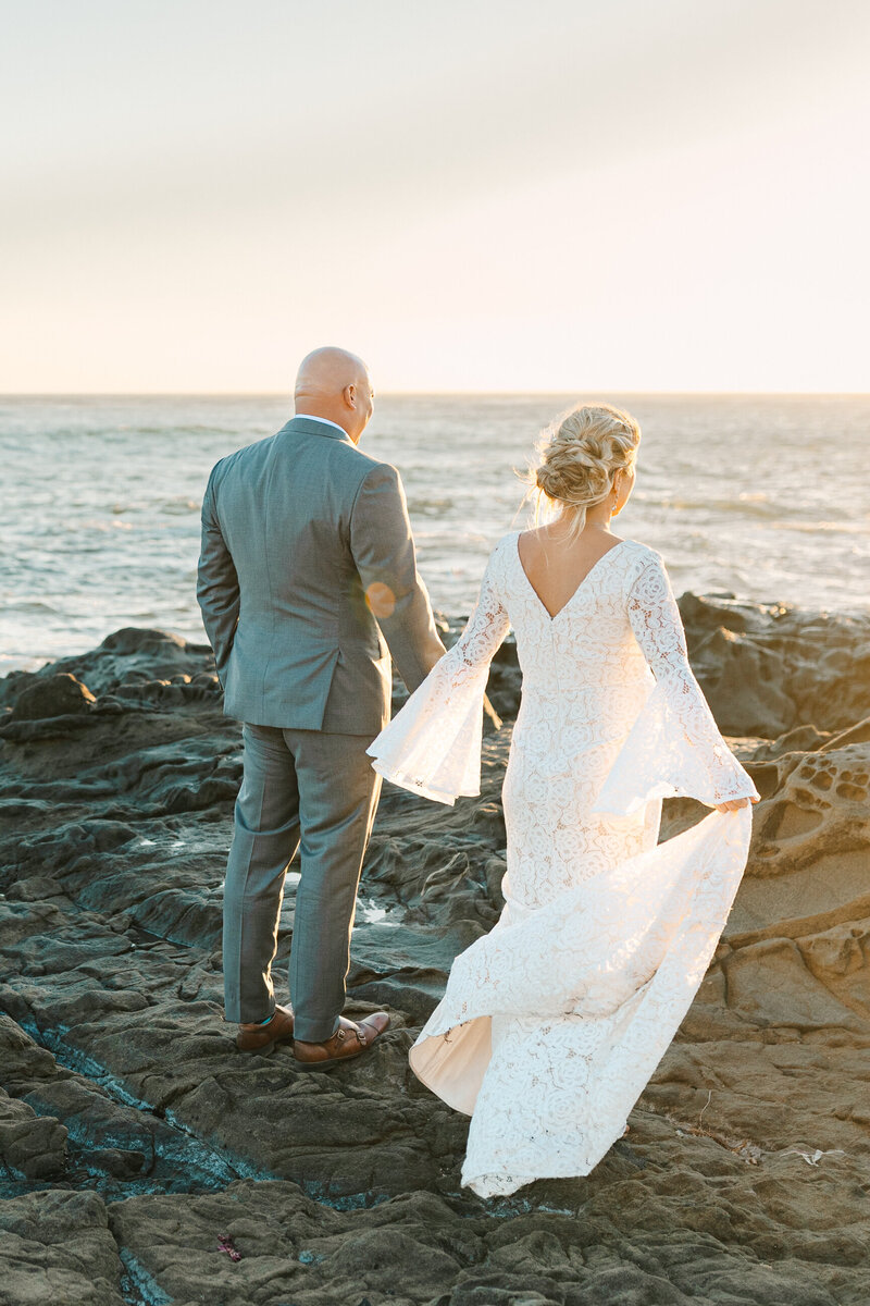 couple embracing near the edge of the cliffside. She is wearing a rust colored lace dress and he is in a beige button up and blue jeans with cowboy boots.