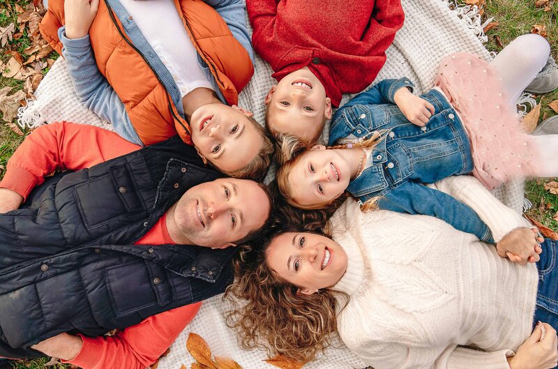 Aerial image. Parents and three children are laying on the ground with their heads touching in a circle. All are looking and smiling at the camera. Captured by Liza Nicole Photography, Philadelphia and Main Line family photographer.