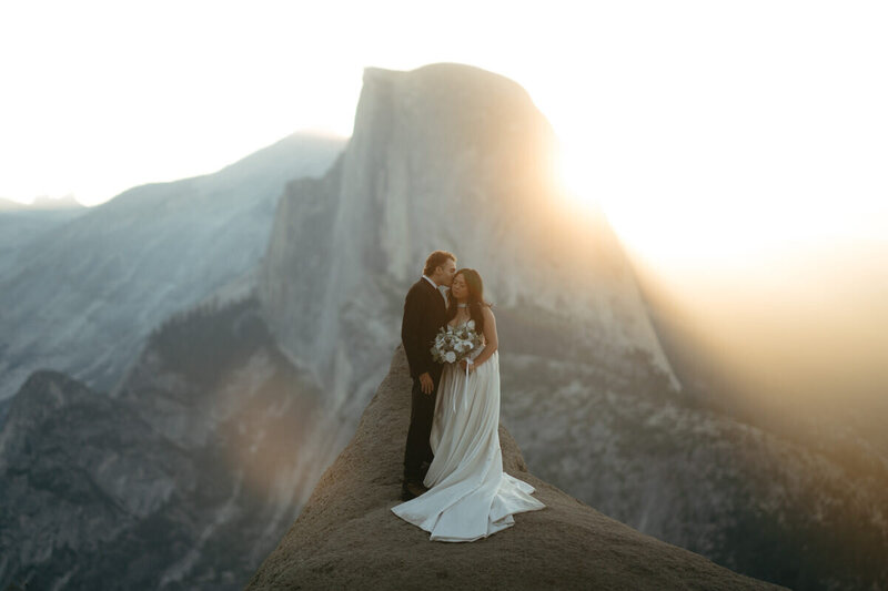 Elopement Photo Ideas | Eloping couple stands on a rock with a majestic Glacier Point sunrise behind them