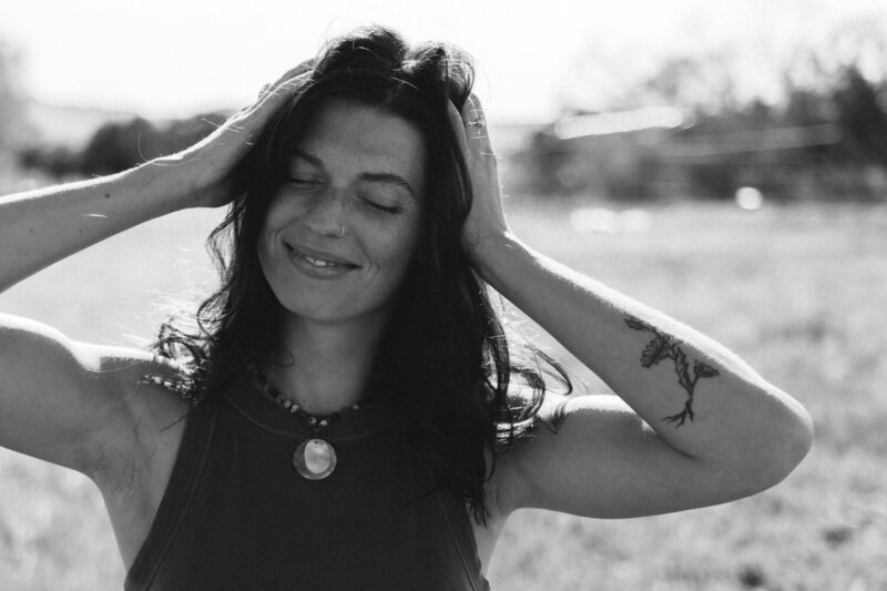 Black and white image of a woman smiling while hair is blowing in the wind an she's trying to fix it