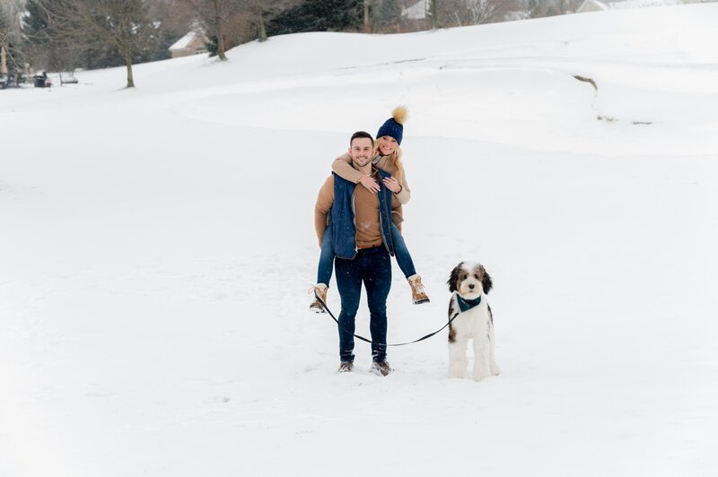 man holding woman with a dog in the snow
