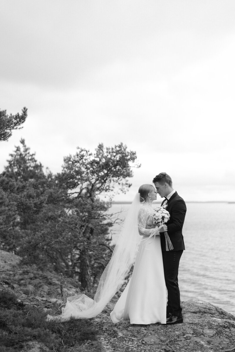 A wedding photo taken by the sea in Turku, Finland. The wedding cople is standing in the rocks in the seaside forest. Romantic wedding portrait taken by wedding photographer Hannika Gabrielsson.