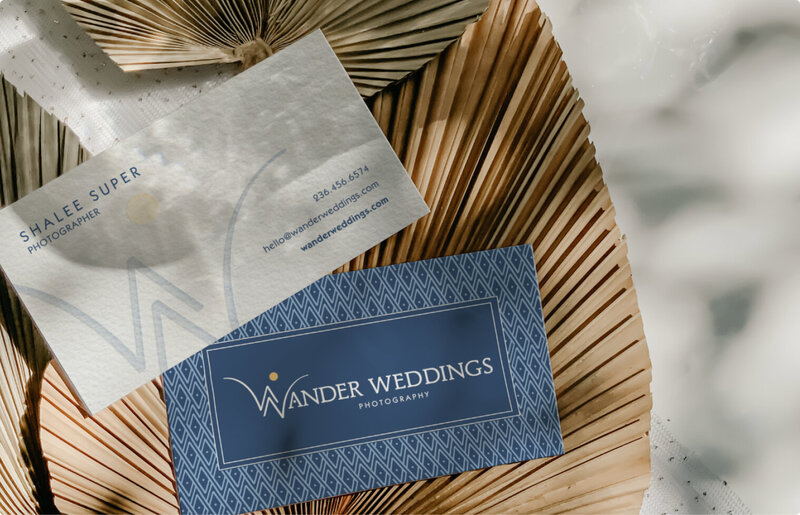 Front and back business card of the brand Wander Weddings laying on top of leafs.