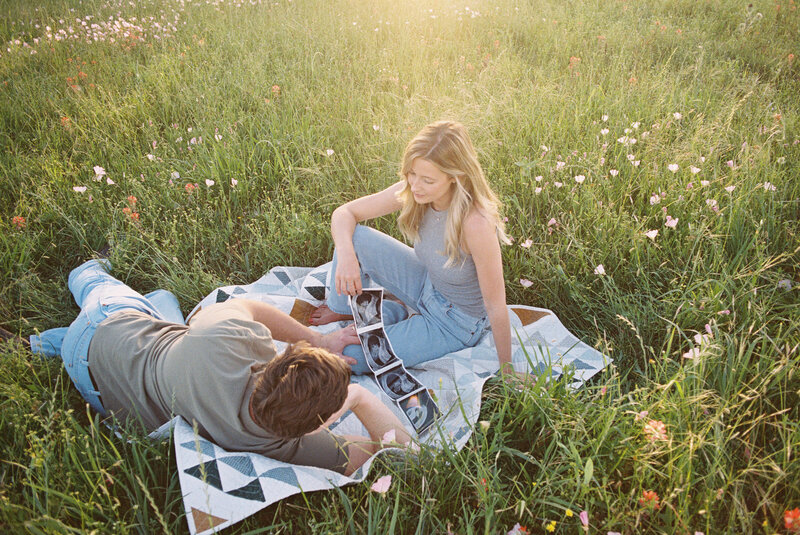 Couple laying on a blanket in the grass holding an ultrasound photo