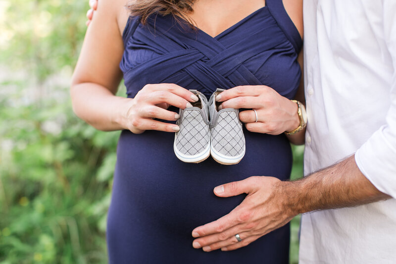 Pregnant woman holding shoes in front of stomach with man's hand holding stomach