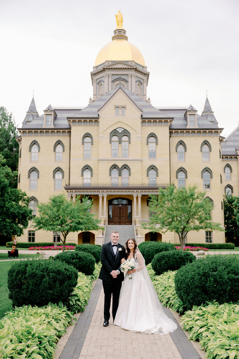 bride and groom posing in front of an ornate building on Notre Dame's campus