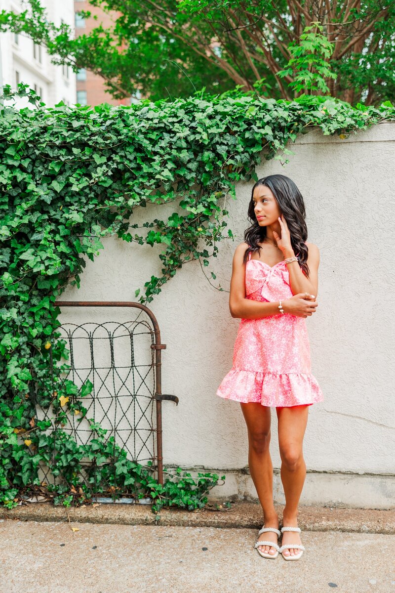 a teenage girl posing by a  wall with greenery