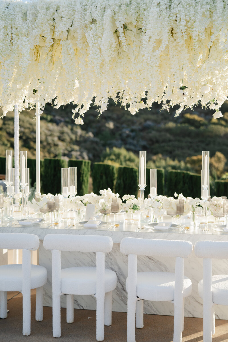 A white marble table with white chairs and white flowers overhanging by luxury wedding planners Passera Events.