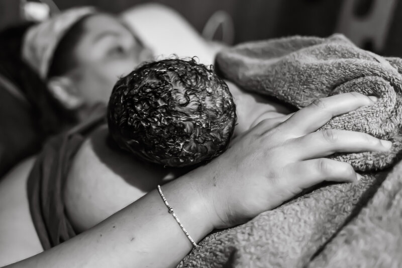 Birth and lifestyle newborn photography in Tifton Georgia of mother holding newborn at breast, showing baby's curly black hair and back of head 