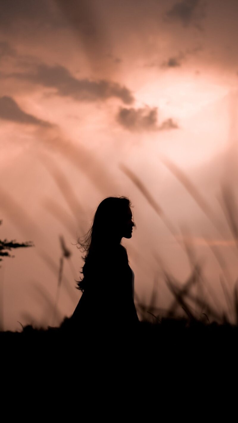 Silhouette of a midlife woman standing on a grass field during sunset, embracing change and new beginnings.