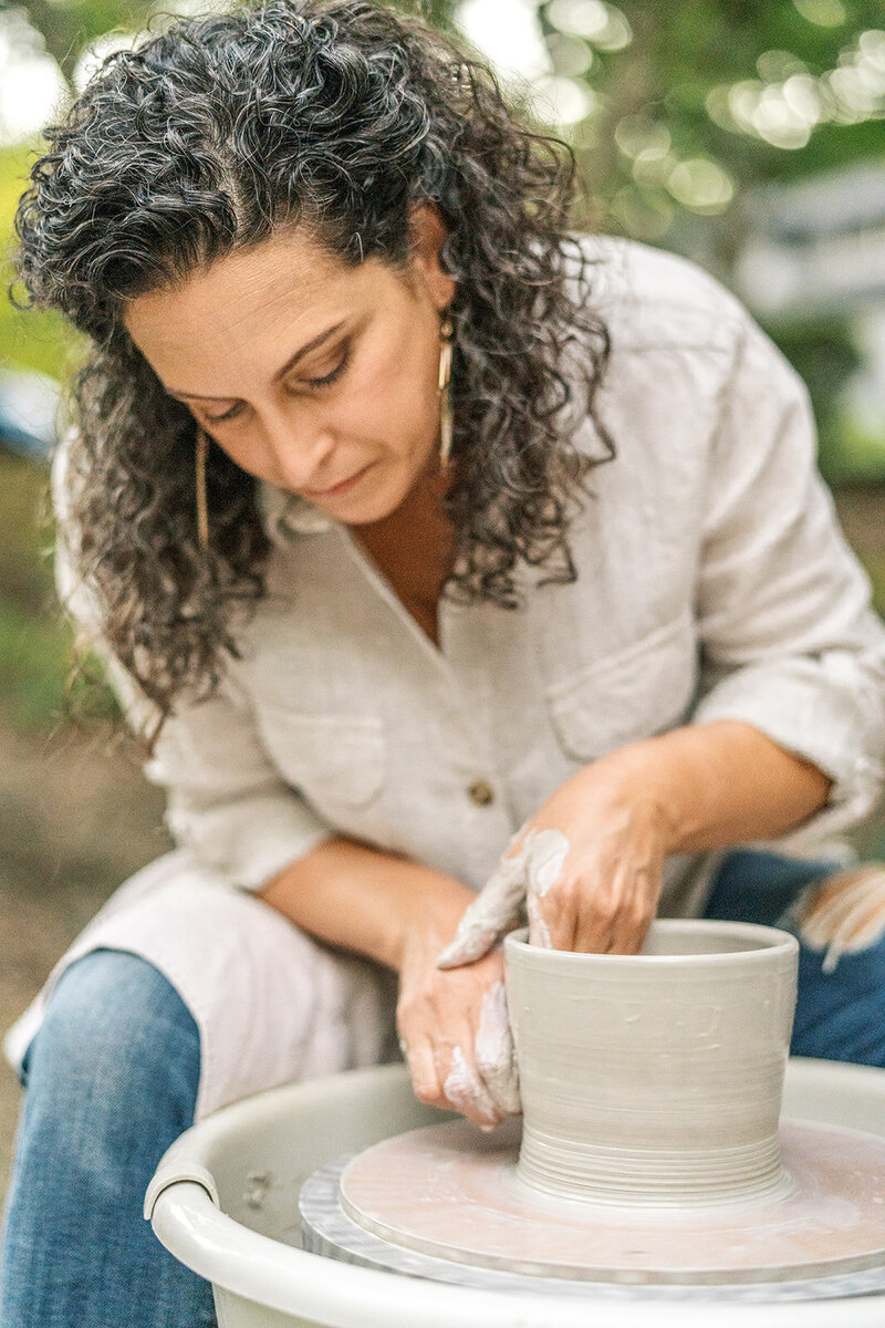 A woman works on creating a pot on a ceramics wheel, representing a branding photo shoot by Among the Oaks. 