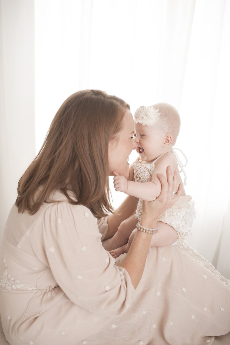 Mother nose to nose with 6 month old daugher in front of window