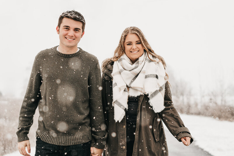Couple holding hands and walking towards the camera as the snow falls.