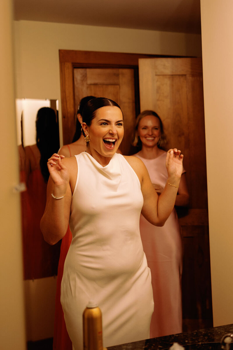Candid photo of beautiful bride looking at herself in the mirror with her reception dress