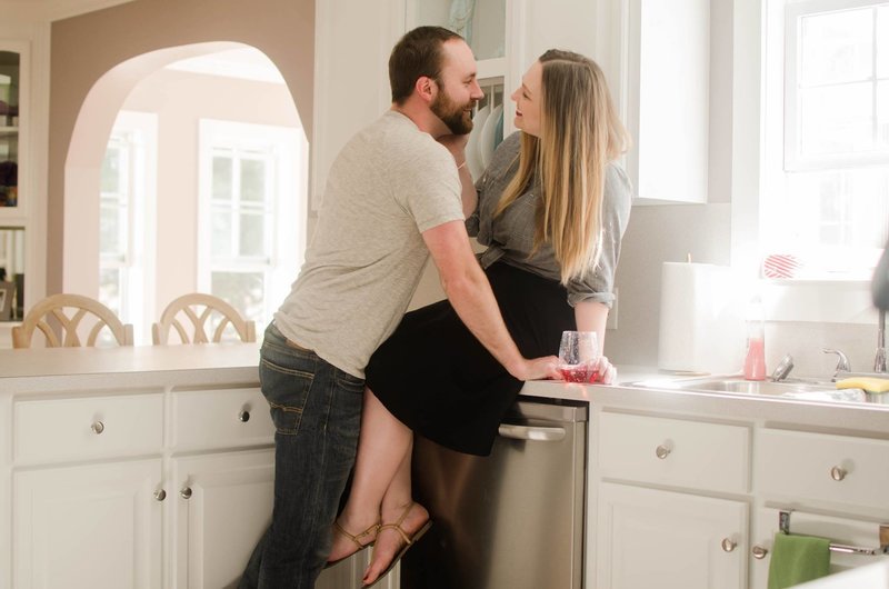 Man leans into woman sitting on kitchen counter