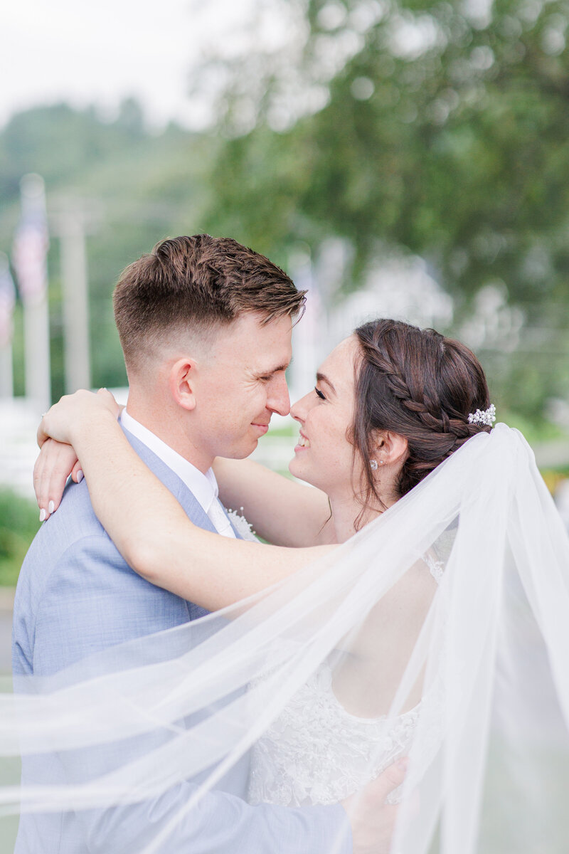 Bride and groom touching noses with veil blowing in the breeze