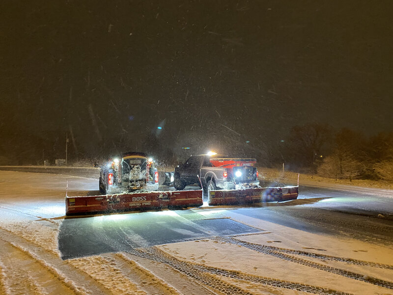 Illuminated snow removal trucks at work during a snowy night