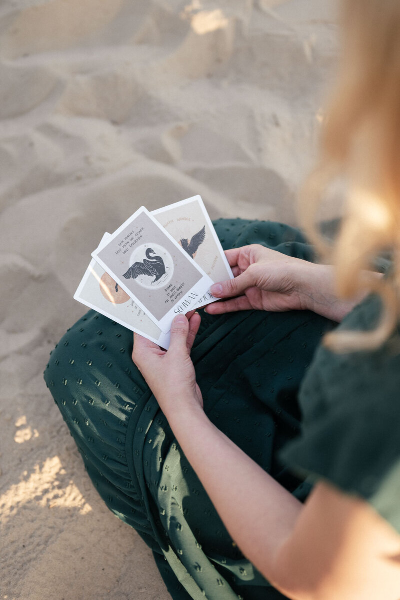 eine Frau hält drei Affirmationskarten im Sand der Boberger Dünen in Hamburg
