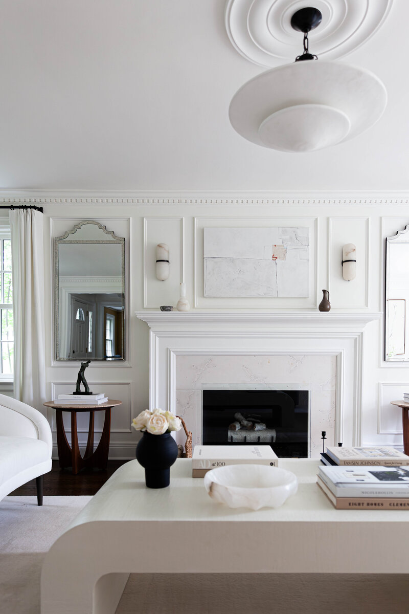 A sophisticated, modern living room designed by Deni + Dove Interiors. The space features elegant millwork, a statement marble fireplace, and carefully curated furnishings in a neutral palette. A sculptural coffee table anchors the room, complemented by layered textures, organic decor, and understated luxury. Thoughtfully styled with curated books, soft florals, and collected objects, this design embodies refined living in Short Hills, Summit, Montclair, Ridgewood, Chatham, Essex Fells, Glen Ridge, Hohokus, Madison, Maplewood, Millburn, Mountain Lakes, and South Orange, NJ.