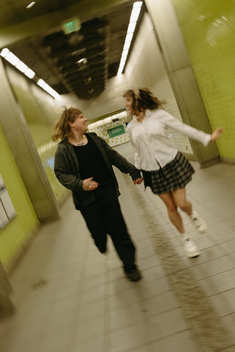 A playful couple runs through a train station during their edgy engagement session